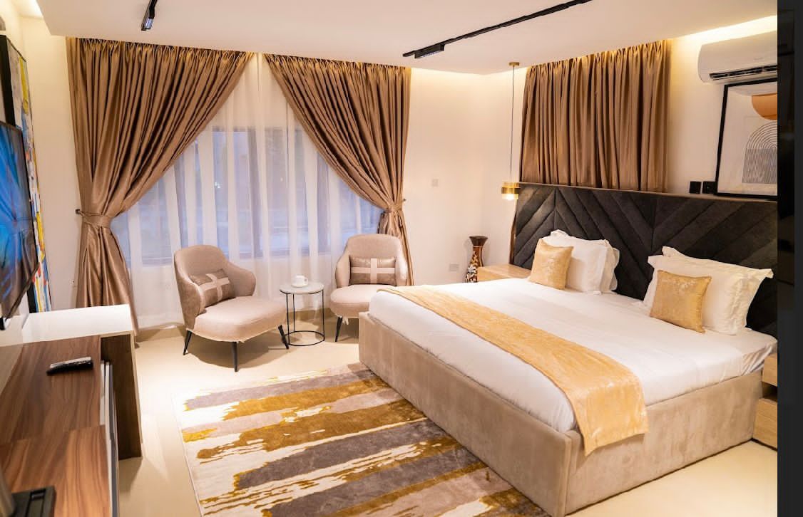 Suite with lounge chairs, bronze drapes and a wide bed